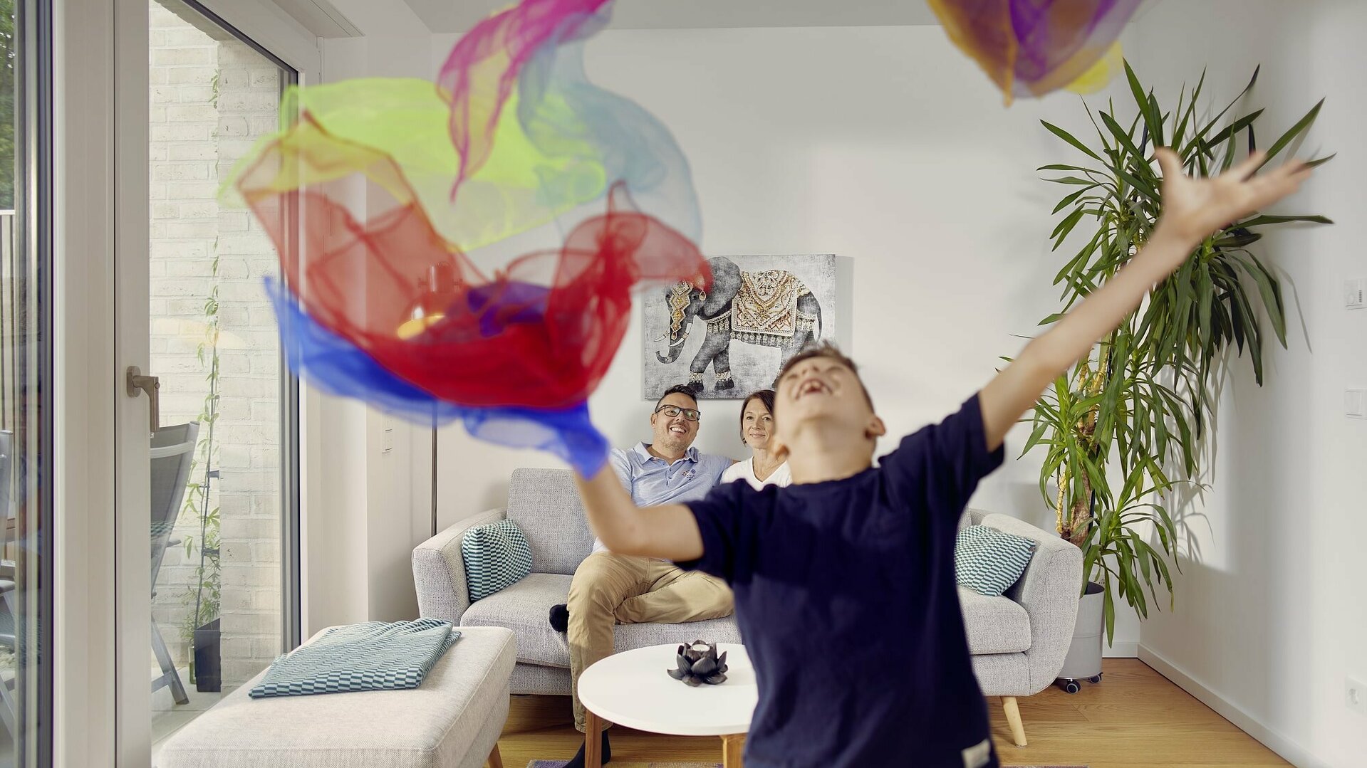 Familie im Reihenhaus Hannover. Junge wirft bunte Tücher in die Luft und freut sich.