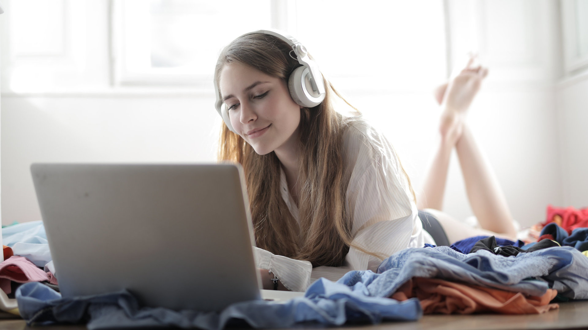 Frau im weißen Shirt, auf dem Sofa, trägt Kopfhörer und bedient MacBook.